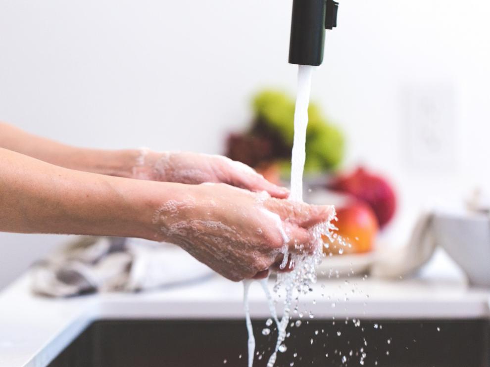 Limpieza de manos en grifo de cocina con alimentos al fondo