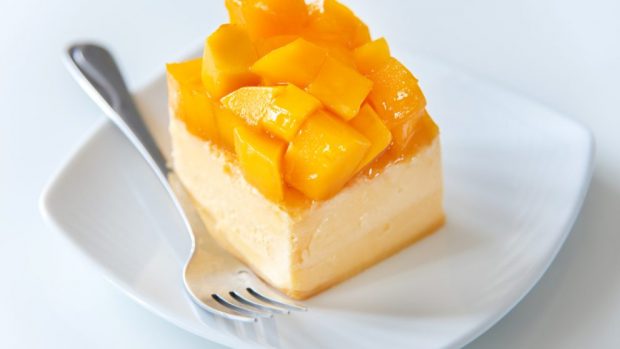 Plato blanco con tenedor de metal con tarta de queso fresco con mango