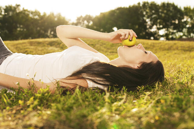 Mujer tumbada en un jardín comiendo una manzana